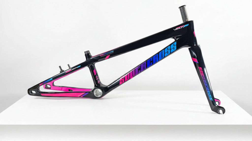 A custom-built BMX bike frame by Super Cross, featuring a glossy black finish with vibrant pink and blue graphics, displayed on a white table.